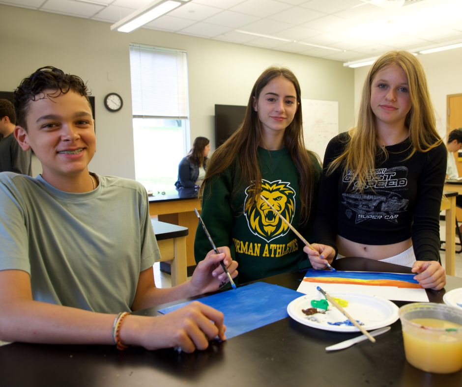 One boy and two girls in classroom with paintbrushes